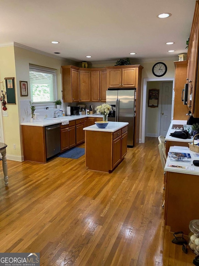 kitchen featuring a kitchen island, wood-type flooring, appliances with stainless steel finishes, crown molding, and sink