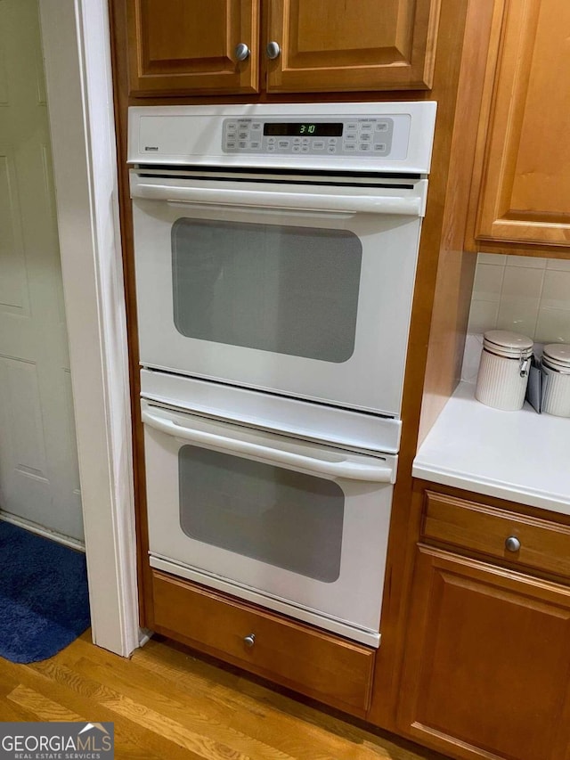 kitchen featuring white double oven, light wood-type flooring, and decorative backsplash