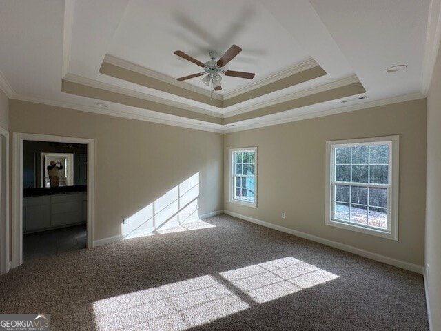 empty room featuring ornamental molding, ceiling fan, dark carpet, and a tray ceiling