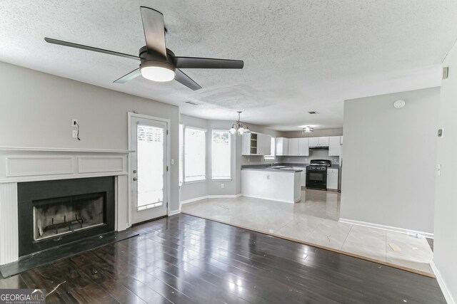 unfurnished living room with a textured ceiling, dark wood-type flooring, and ceiling fan with notable chandelier