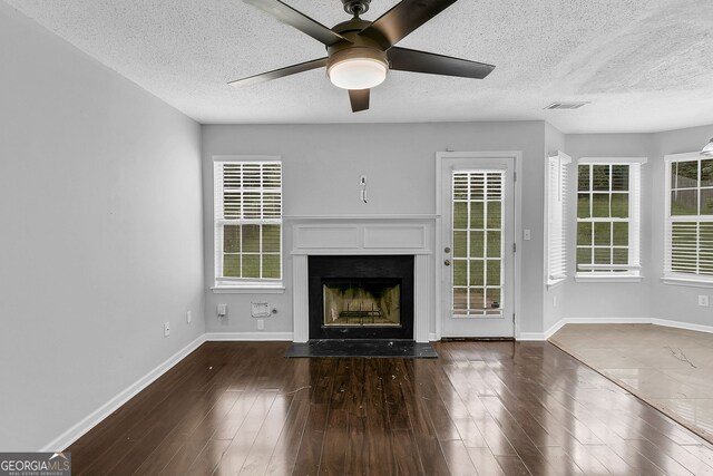 unfurnished living room featuring ceiling fan, plenty of natural light, dark hardwood / wood-style flooring, and a textured ceiling