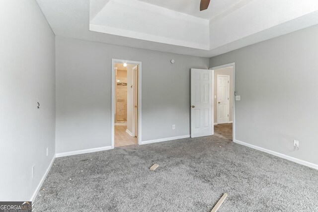 unfurnished bedroom featuring a raised ceiling, connected bathroom, ceiling fan, and carpet