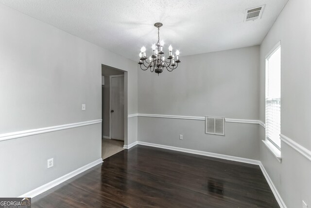 spare room with dark hardwood / wood-style floors, an inviting chandelier, and a textured ceiling