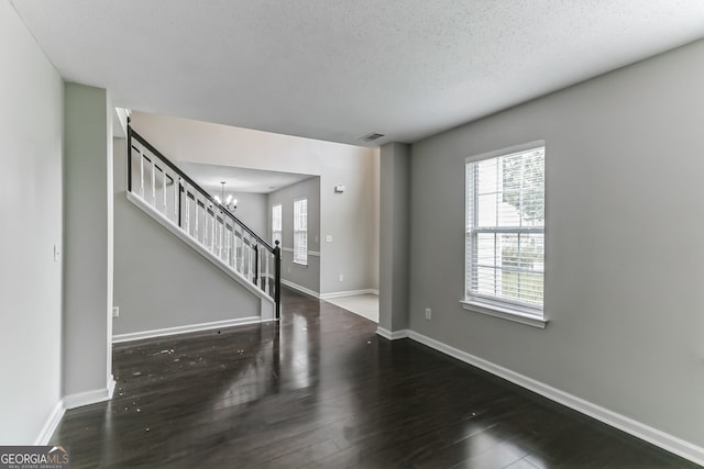 spare room with a textured ceiling, dark wood-type flooring, and a notable chandelier