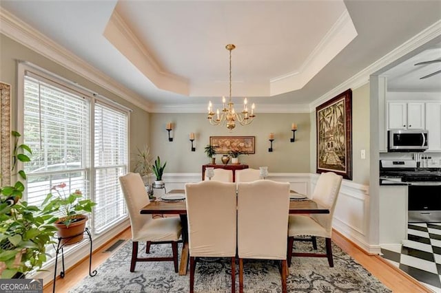 dining space featuring light wood-type flooring, a tray ceiling, crown molding, and a notable chandelier