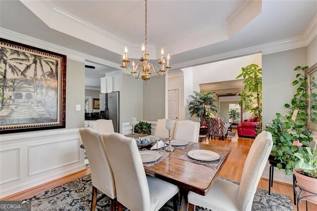 dining area featuring ornamental molding, a raised ceiling, a notable chandelier, and light hardwood / wood-style floors