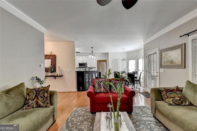 living room with crown molding, ceiling fan with notable chandelier, and light wood-type flooring