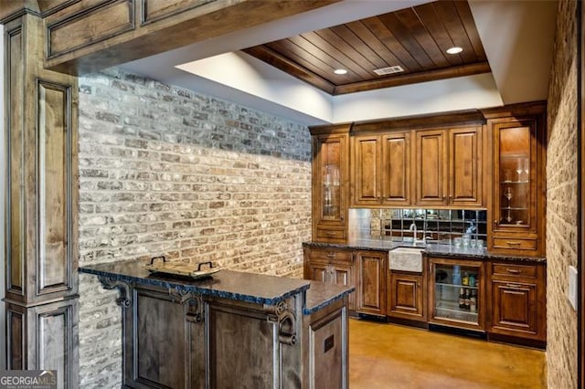 kitchen featuring dark stone countertops, wine cooler, a tray ceiling, wood ceiling, and brick wall