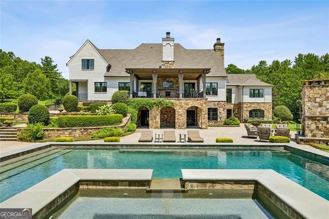 rear view of property featuring a patio and a pool with hot tub