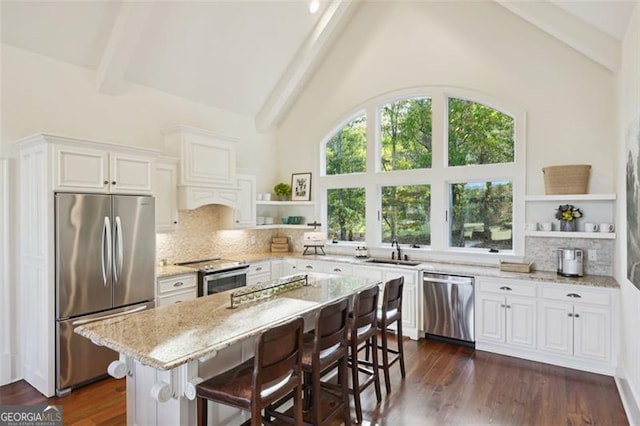 kitchen featuring light stone countertops, beam ceiling, a center island, stainless steel appliances, and dark wood-type flooring