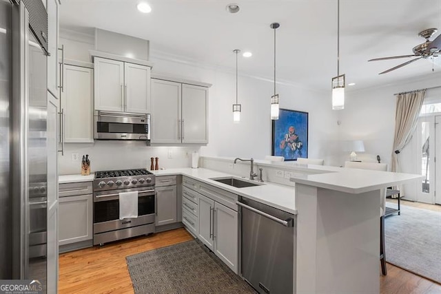 kitchen featuring high quality appliances, kitchen peninsula, sink, ceiling fan, and light wood-type flooring