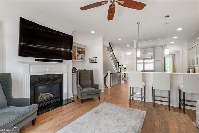 living room featuring ceiling fan, ornamental molding, and light hardwood / wood-style flooring