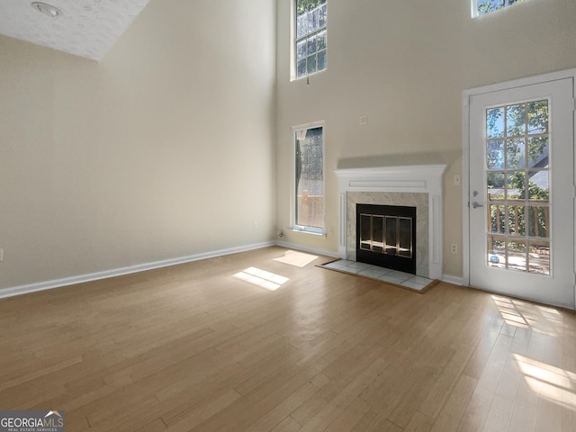 unfurnished living room featuring baseboards, a healthy amount of sunlight, a premium fireplace, and light wood-style floors