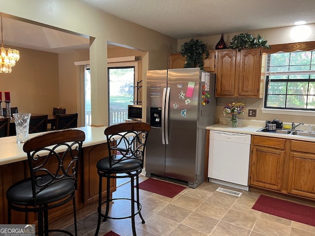 kitchen with dishwasher, a chandelier, sink, a breakfast bar area, and stainless steel fridge with ice dispenser