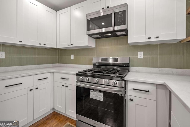 kitchen featuring light wood-type flooring, appliances with stainless steel finishes, light stone countertops, white cabinetry, and decorative backsplash