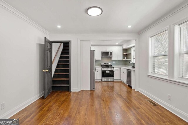 kitchen with appliances with stainless steel finishes, tasteful backsplash, dark wood-type flooring, ornamental molding, and white cabinetry