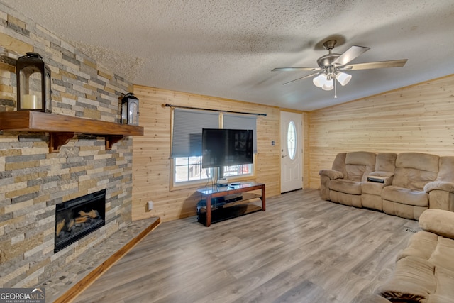 living room featuring a textured ceiling, ceiling fan, a stone fireplace, and hardwood / wood-style flooring