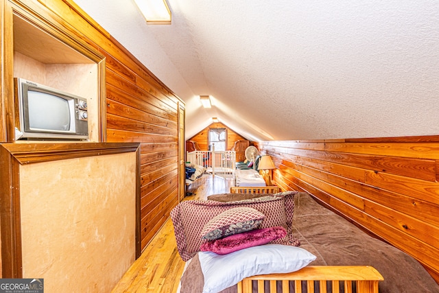 bedroom with a textured ceiling, vaulted ceiling, wood walls, and hardwood / wood-style flooring