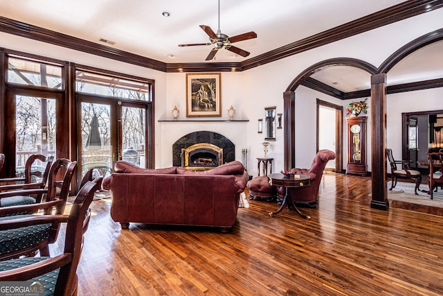 living room with dark wood-type flooring, ceiling fan, crown molding, and a high end fireplace