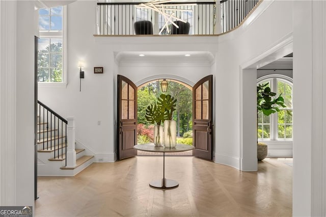 entrance foyer featuring light parquet floors, plenty of natural light, a towering ceiling, and crown molding