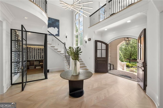 foyer with light parquet flooring, ornamental molding, a towering ceiling, and a healthy amount of sunlight