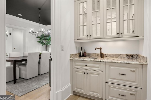 bar featuring light wood-type flooring, pendant lighting, sink, an inviting chandelier, and light stone countertops