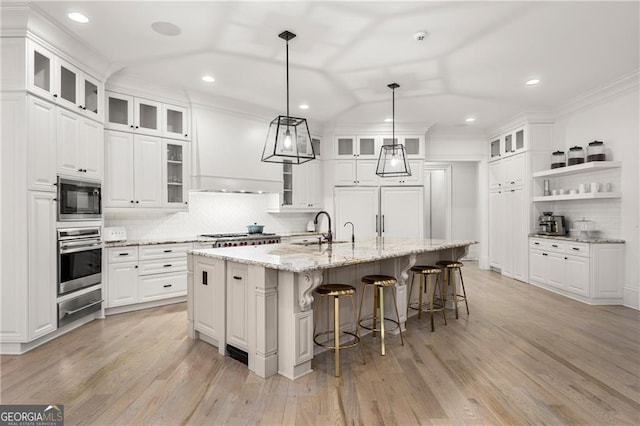 kitchen featuring light wood-type flooring, stainless steel appliances, white cabinetry, a breakfast bar area, and a center island with sink