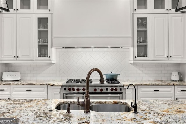 kitchen with high end stainless steel range oven, light stone counters, decorative backsplash, and white cabinetry