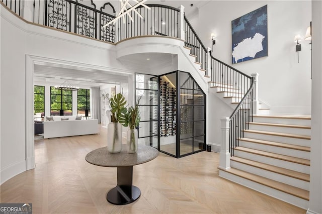 foyer featuring a high ceiling, an inviting chandelier, light parquet floors, and ornamental molding