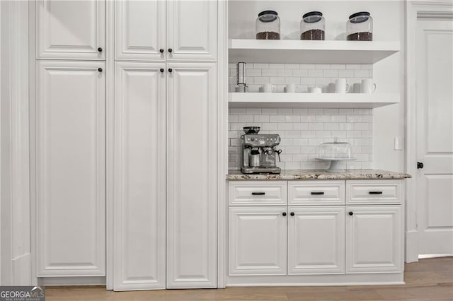 bar featuring light stone countertops, light wood-type flooring, white cabinetry, and decorative backsplash