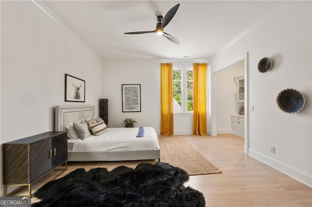 bedroom featuring a walk in closet, ceiling fan, ornamental molding, and light wood-type flooring