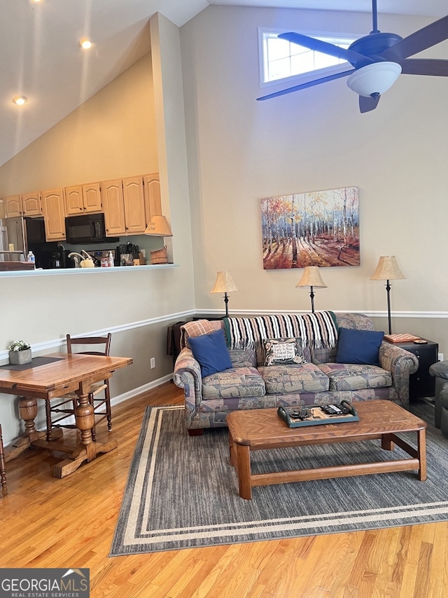 living room with high vaulted ceiling, ceiling fan, and light wood-type flooring