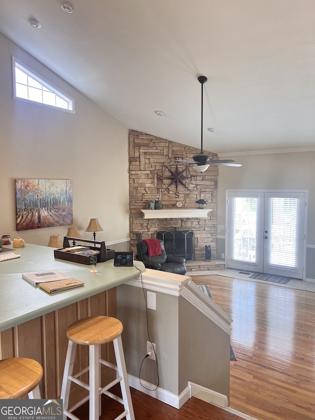 kitchen featuring wood-type flooring, ceiling fan, vaulted ceiling, and a stone fireplace