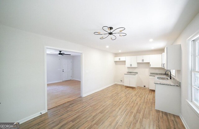 kitchen with white cabinets, light wood-type flooring, ceiling fan with notable chandelier, light stone counters, and sink