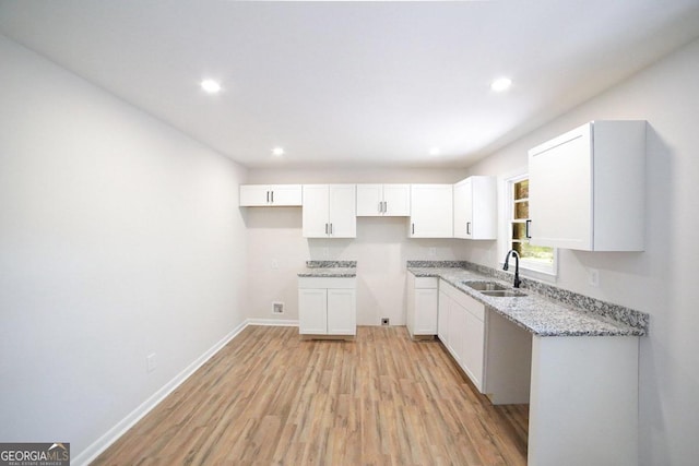 kitchen with light hardwood / wood-style flooring, light stone counters, sink, and white cabinetry