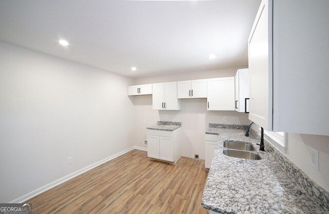 kitchen featuring light wood-type flooring, light stone counters, sink, and white cabinets