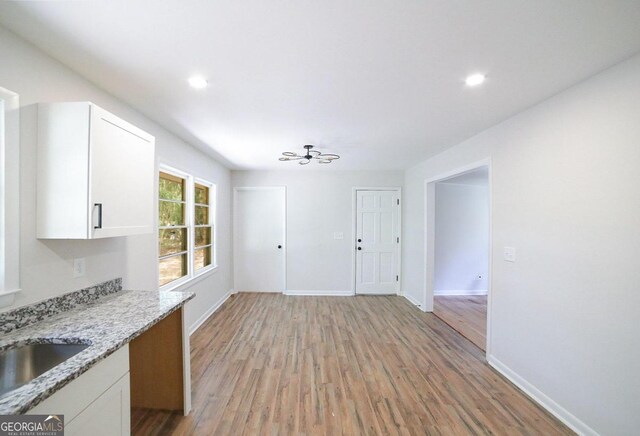 kitchen featuring light stone counters, sink, light wood-type flooring, and white cabinetry