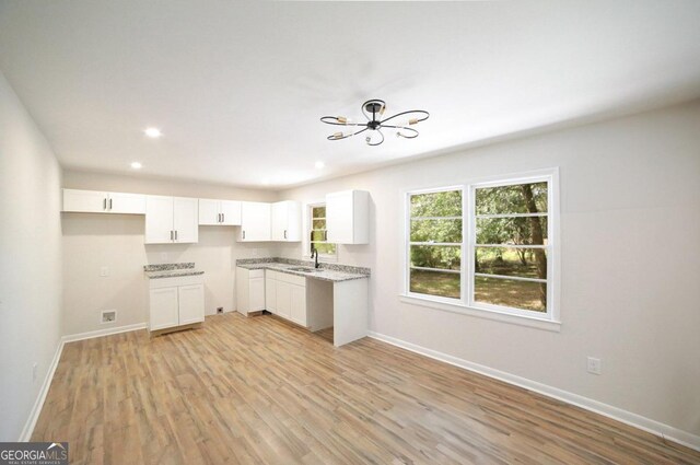 kitchen featuring light stone countertops, a chandelier, light hardwood / wood-style floors, white cabinetry, and sink