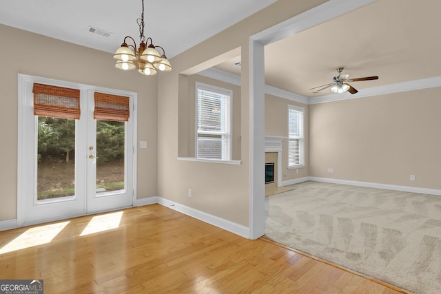 unfurnished living room with ornamental molding, ceiling fan with notable chandelier, light wood-type flooring, and french doors