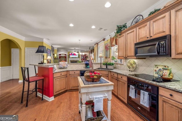 kitchen featuring a kitchen island, light stone countertops, black appliances, light hardwood / wood-style floors, and a kitchen bar