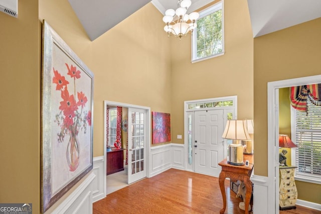 entryway with high vaulted ceiling, plenty of natural light, a chandelier, and wood-type flooring