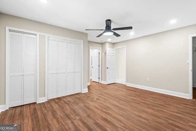 unfurnished bedroom with two closets, ceiling fan, and hardwood / wood-style flooring