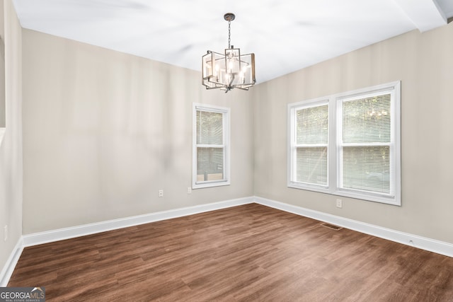 unfurnished room with a healthy amount of sunlight, a chandelier, and dark hardwood / wood-style flooring