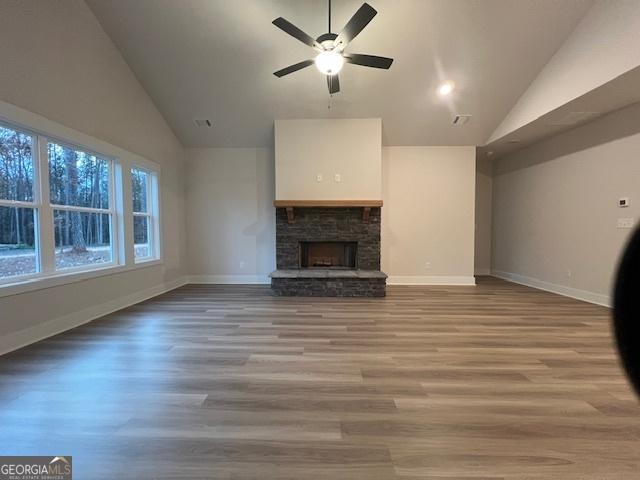 unfurnished living room with hardwood / wood-style floors, ceiling fan, a fireplace, and high vaulted ceiling