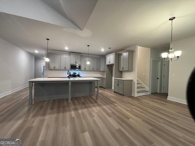 kitchen featuring gray cabinetry, an island with sink, pendant lighting, appliances with stainless steel finishes, and hardwood / wood-style flooring