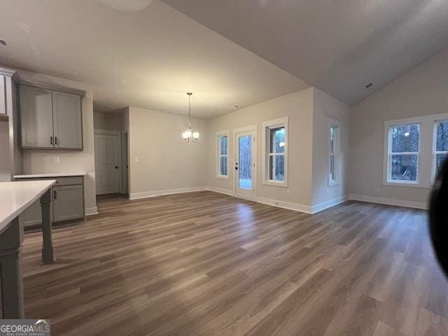 unfurnished living room with dark wood-type flooring, vaulted ceiling, and an inviting chandelier