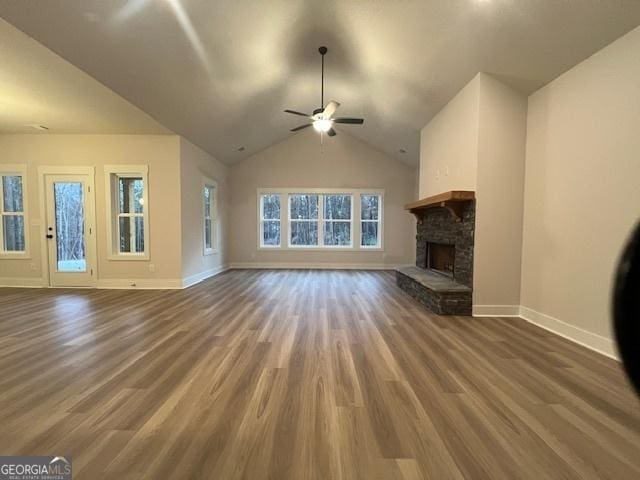 unfurnished living room with dark hardwood / wood-style floors, ceiling fan, a stone fireplace, and lofted ceiling