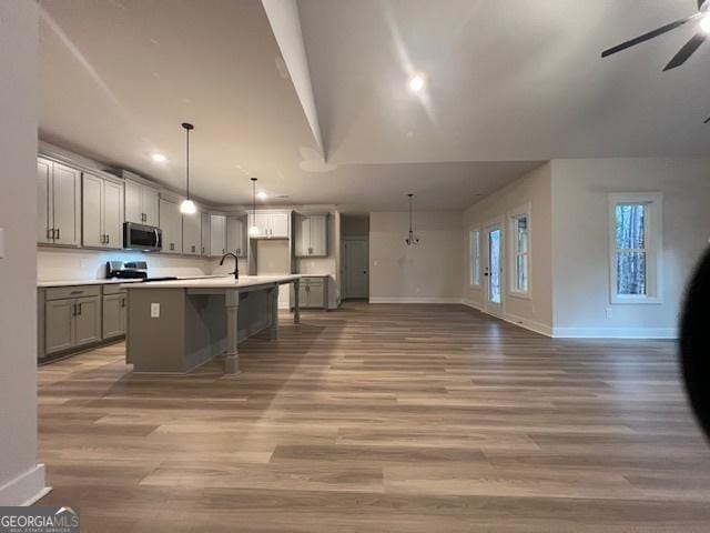 kitchen with hanging light fixtures, hardwood / wood-style floors, stainless steel appliances, and a kitchen island with sink