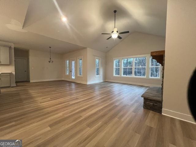 unfurnished living room with ceiling fan with notable chandelier, lofted ceiling, and hardwood / wood-style flooring