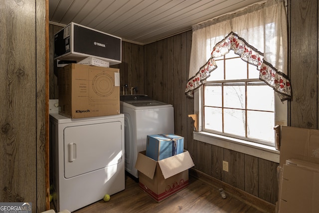 laundry area with plenty of natural light, wood walls, wood-type flooring, and washing machine and clothes dryer